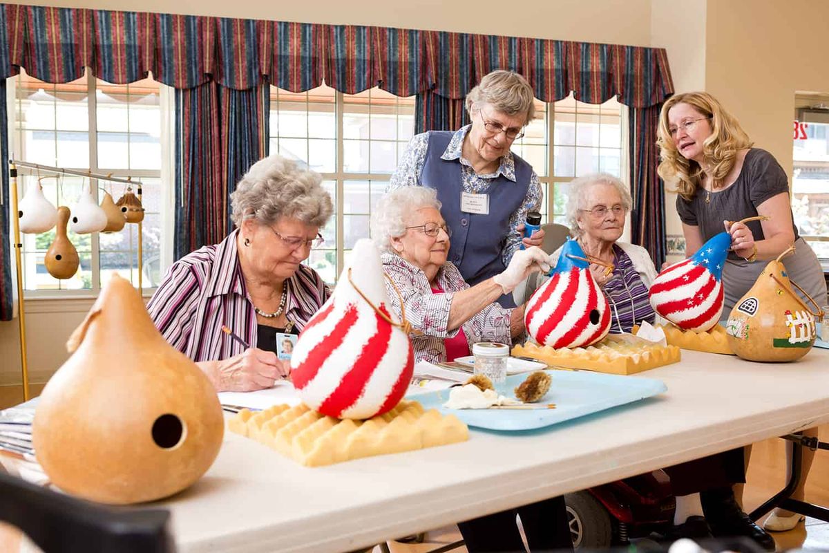 A group of seniors enjoying a crafting session, painting gourds with stripes in an art class.