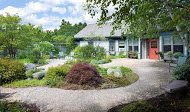A charming house surrounded by a lush garden with winding pathways and various plants.