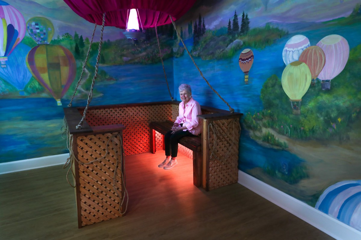 A woman seated in a creatively decorated room with a mural of hot air balloons and colorful lighting.