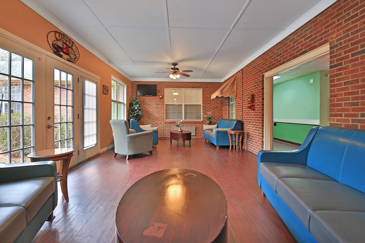 A cozy living room with brick walls, featuring several chairs and a coffee table, illuminated by natural light through large windows.