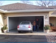 A car parked in a residential garage with two people standing inside.