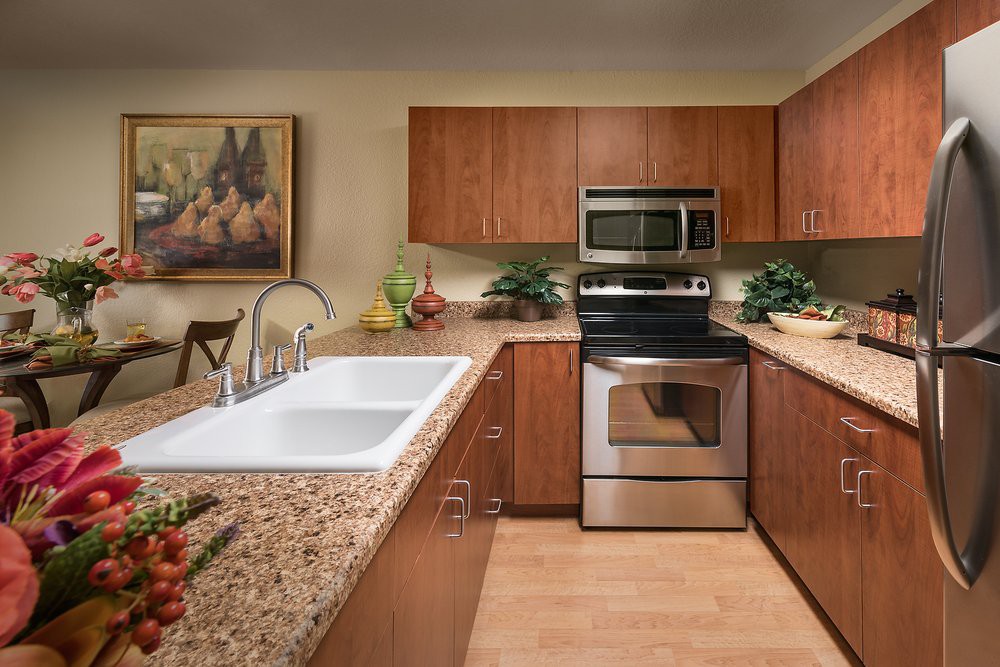 A modern kitchen with wooden cabinets and granite countertops, featuring a double sink, oven, and microwave.