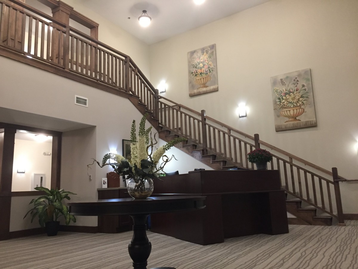 A spacious lobby with a wooden staircase, decorative plants, and wall artwork.