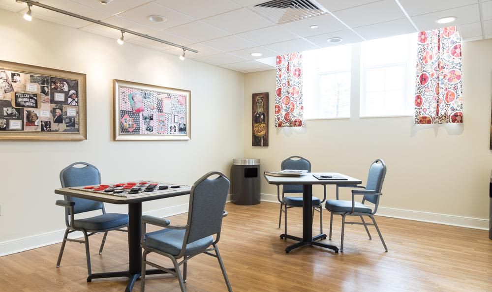 A recreation room with tables and chairs, featuring a checkers game and artwork on the walls.