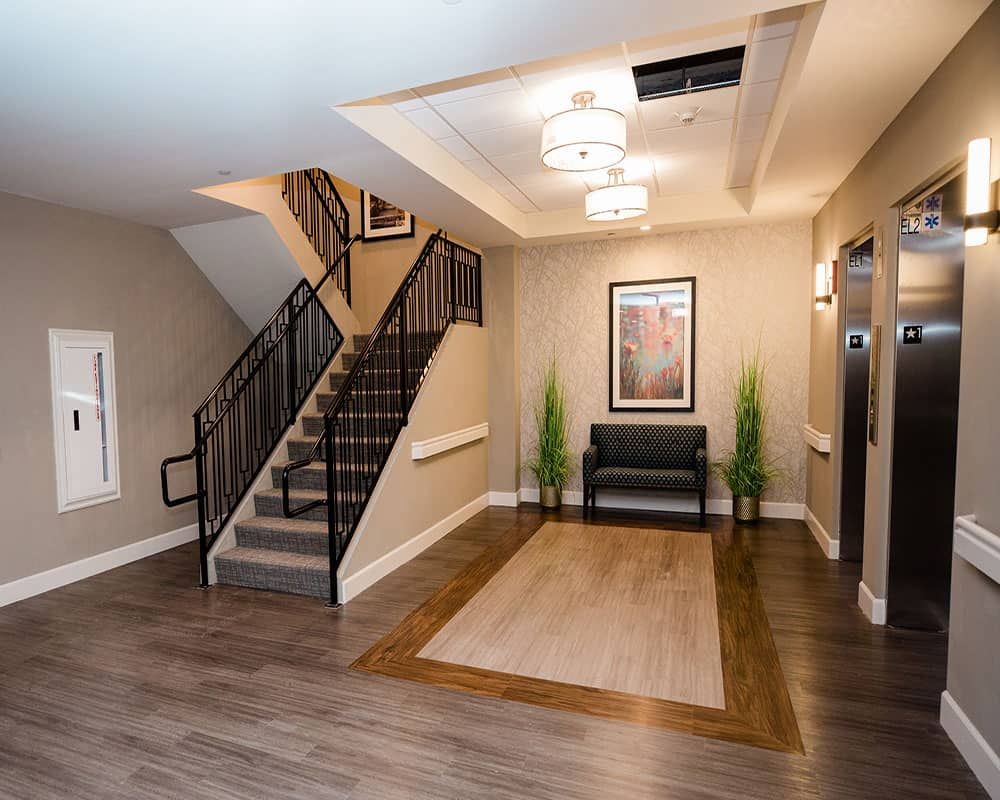 A modern lobby area featuring a staircase, elevator, and seating with decorative plants and artwork.