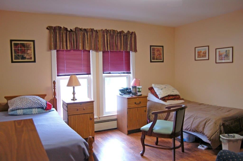 A cozy bedroom with two single beds, nightstands, and a chair by the windows.