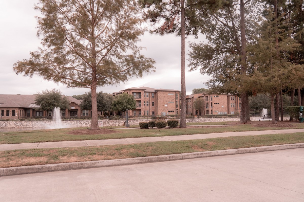 A view of an apartment complex with a fountain surrounded by trees on a cloudy day.