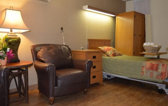 A cozy hospital room featuring an armchair next to a bed and nightstand.