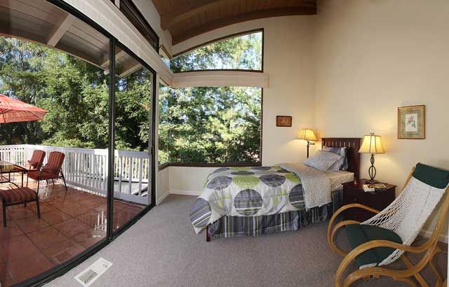 A cozy bedroom with large windows overlooking trees, allowing natural light to fill the modern interior.