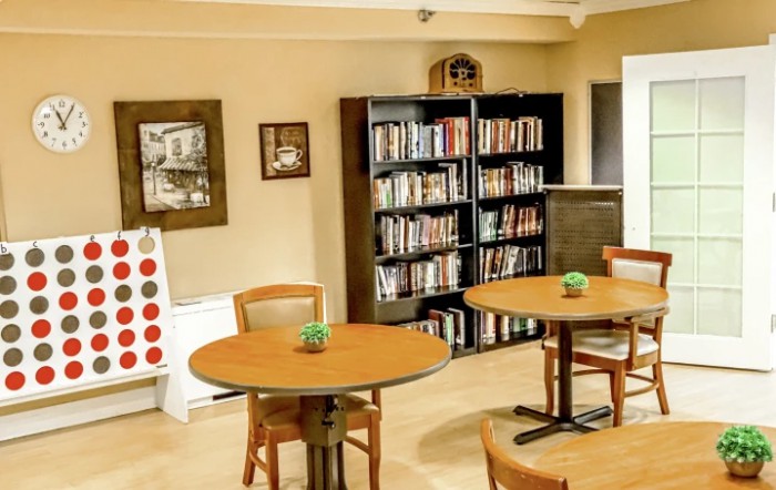 A cozy library space with bookshelves, tables, and chairs for reading.