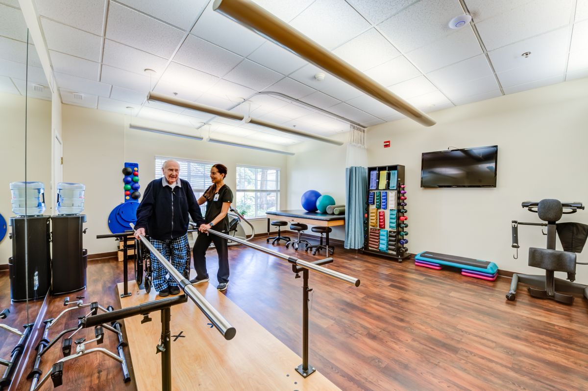 A therapist assists an elderly patient during a physical rehabilitation session in a medical facility equipped with exercise tools.