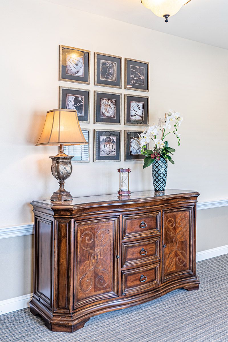 A stylish wooden dresser topped with a lamp and a vase of flowers, set against a wall adorned with decorative framed art.