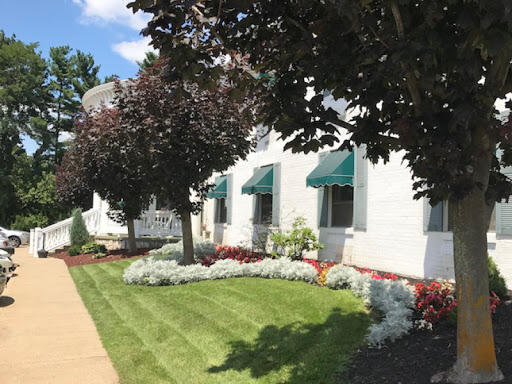 A well-maintained building exterior featuring lush landscaping and green awnings on a sunny day.