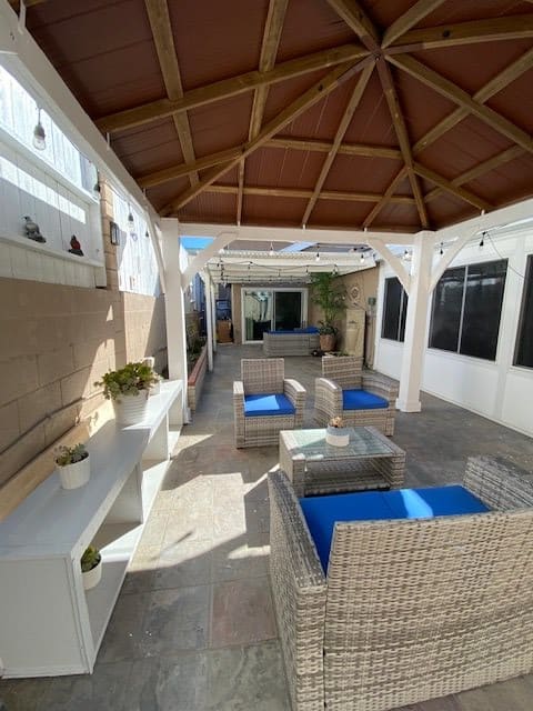 A modern outdoor patio with wicker furniture and a wooden pergola, bathed in sunlight.