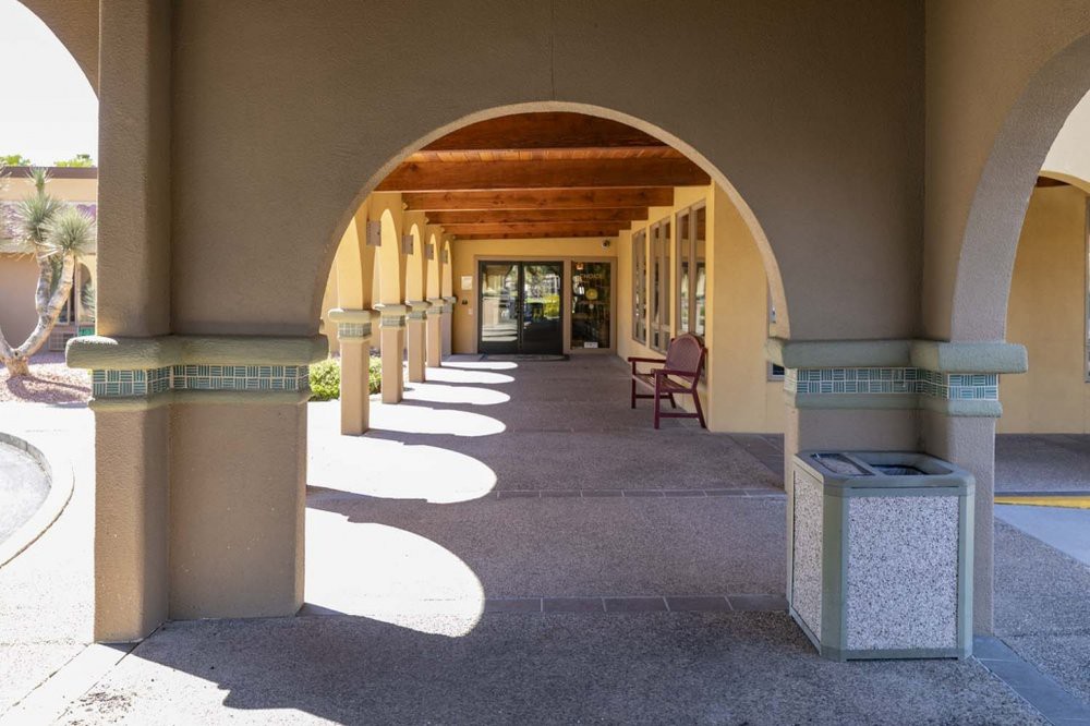 A sunny corridor with archways and columns creating shadows on the ground.