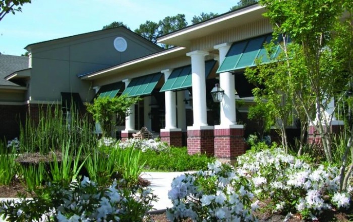 A scenic view of a building with columns and green awnings, surrounded by lush garden landscaping.