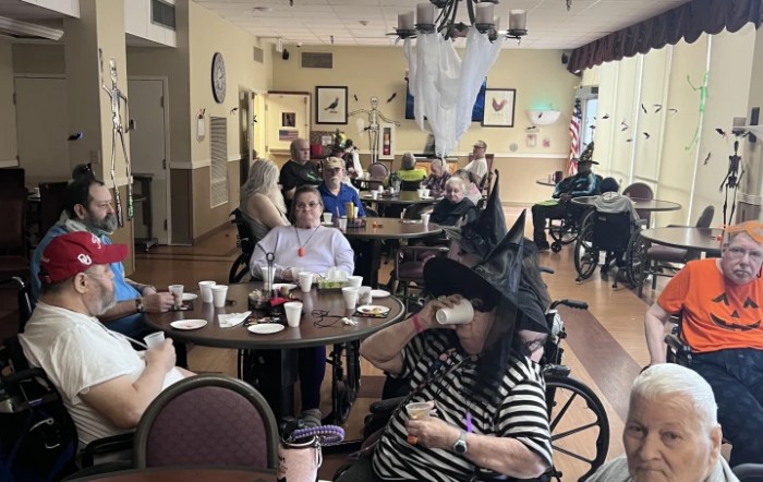 Residents at a nursing home enjoy a Halloween celebration, with one person wearing a witch hat.