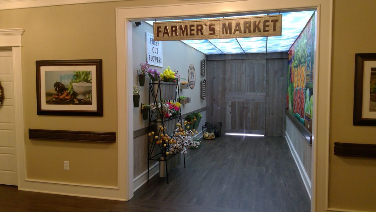 An indoor setup resembling a farmer's market with floral decor and a signage overhead.