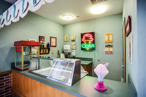 A cozy ice cream shop interior featuring a vibrant neon 'Open' sign and an inviting display counter.