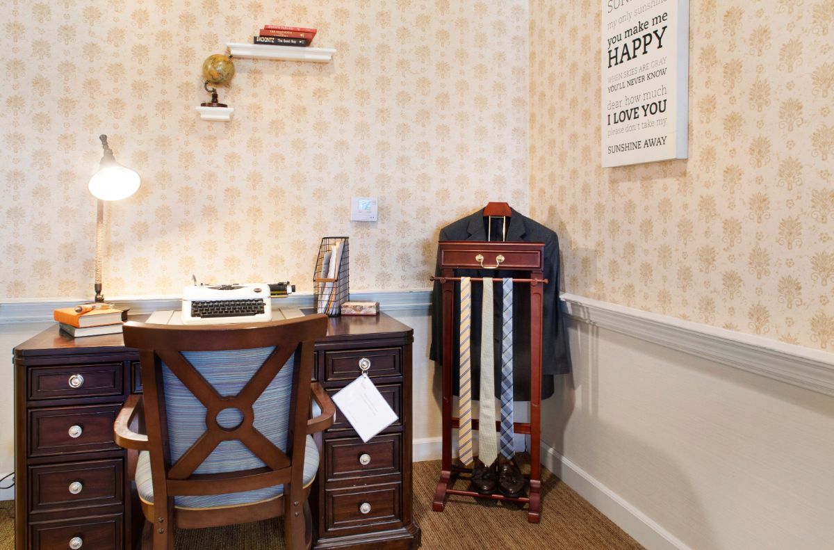 A vintage-style office corner with a wooden desk, chair, and suit stand.