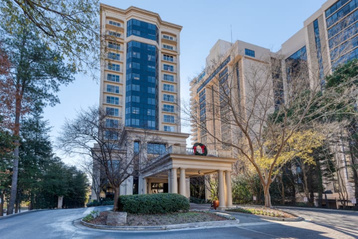 A tall hotel building with a welcoming entrance surrounded by trees.