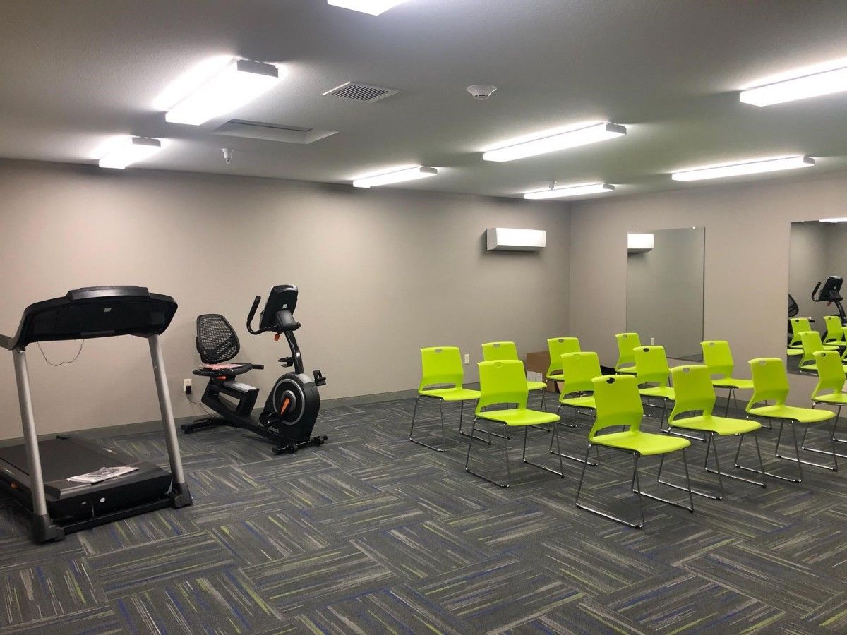 A multi-purpose room with gym equipment and arranged chairs.