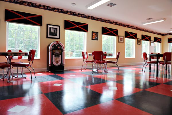 A retro-themed diner with red and black checkered flooring, a vintage jukebox, and empty seating.