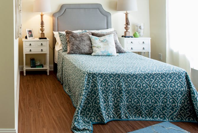A cozy bedroom featuring a neatly made bed with patterned bedding, flanked by nightstands and lamps.