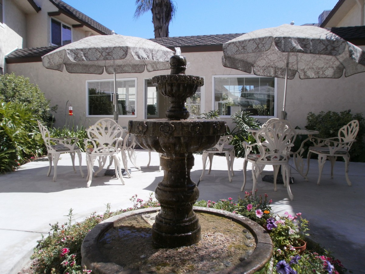 A peaceful outdoor patio featuring a central fountain surrounded by chairs, tables, and umbrellas.
