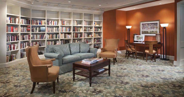 A cozy library room with a sofa, chairs, and bookshelves filled with books.