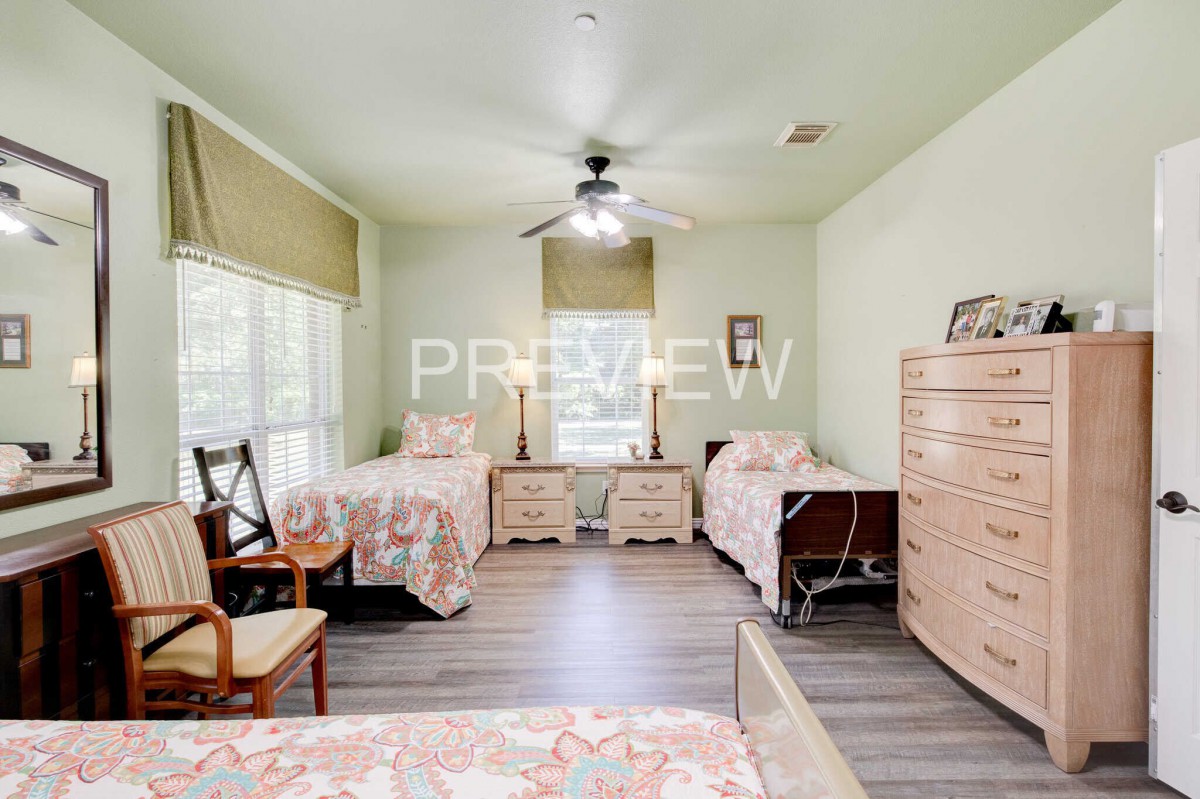 A cozy bedroom with twin beds, a dresser, chairs, and large windows letting in natural light.