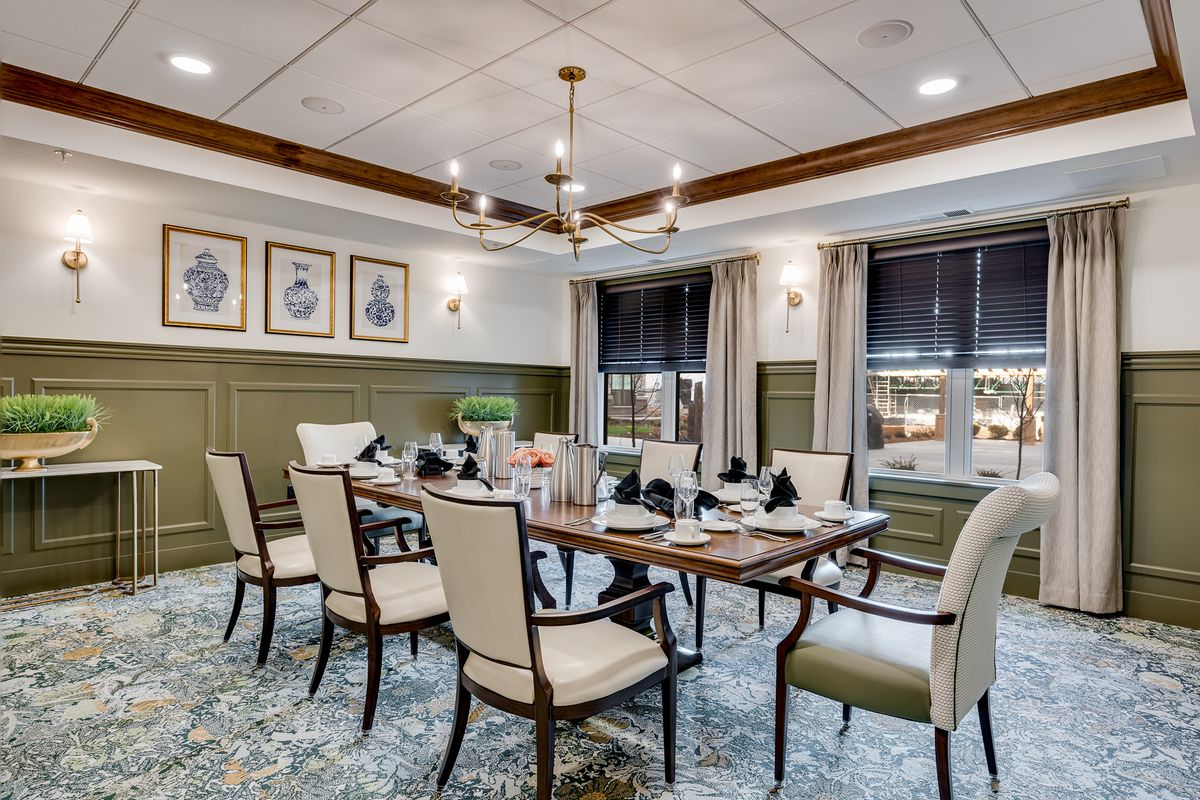 An elegantly designed dining room featuring a large table, comfortable chairs, and a modern chandelier, with artwork adorning the walls.