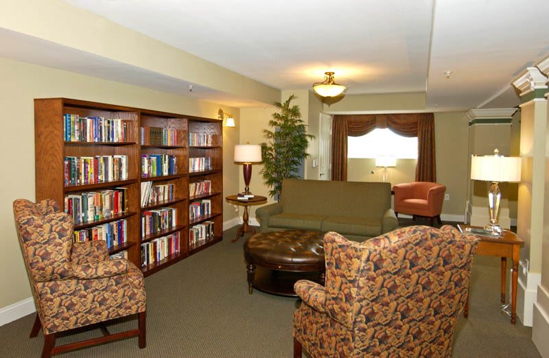 A cozy library with bookshelves, armchairs, and a warm reading area.