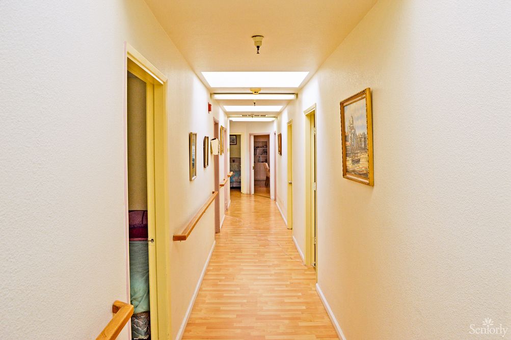 A well-lit hallway with a wooden floor, lined with doors and decorated with paintings.