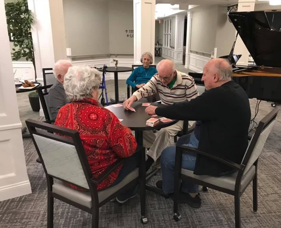 A group of seniors gathered around a table playing cards together.
