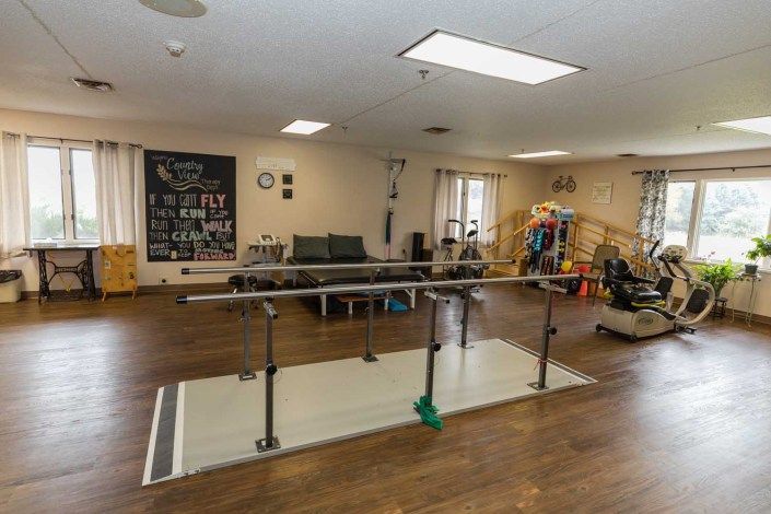 A rehabilitation room equipped with parallel bars and various exercise equipment.