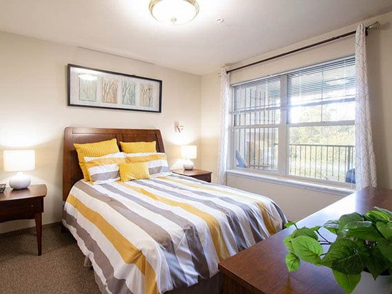 A cozy bedroom with striped bedding and natural light from a large window.