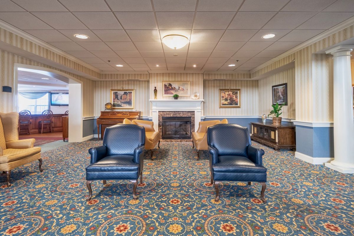 A traditional living room with blue chairs, a patterned carpet, and a fireplace.