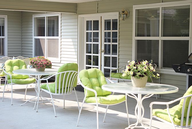 A cozy patio with green-cushioned chairs, tables, and potted flowers.