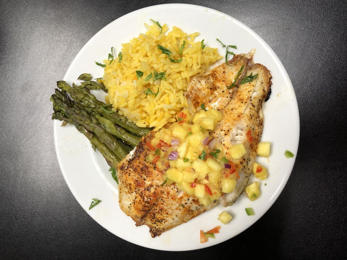A delicious plate featuring grilled chicken topped with mango salsa, served alongside yellow rice and asparagus.