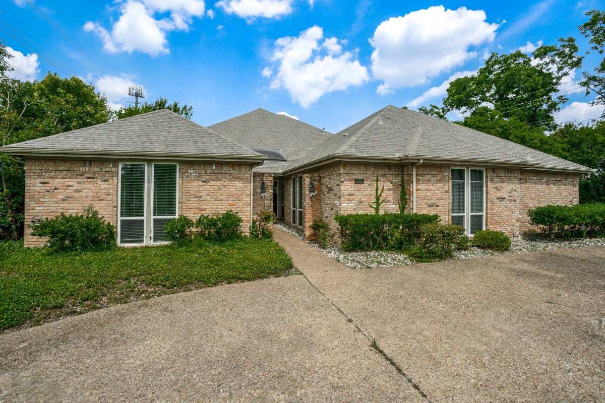 A brick residential house with a driveway under a partly cloudy sky.