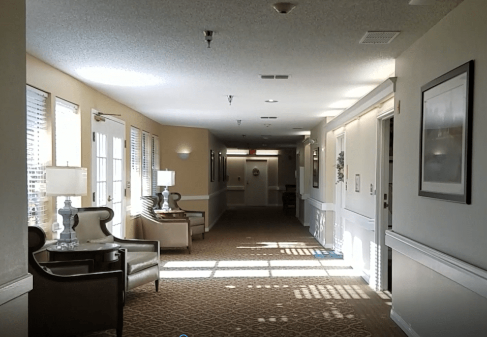 A brightly lit hallway with seating and lamps, featuring a carpeted floor and multiple doors.