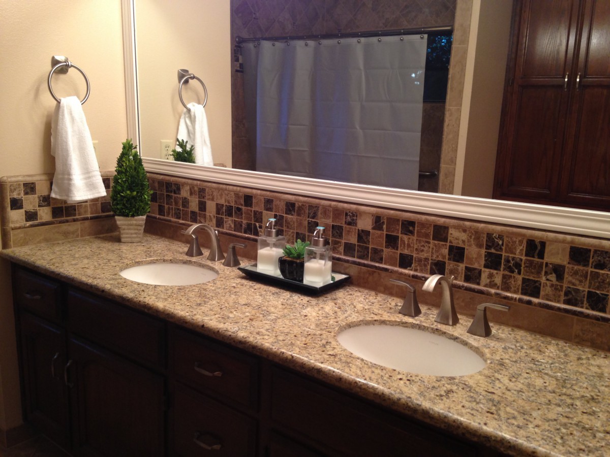 A modern bathroom with a double sink vanity featuring a granite countertop and decorative plants.