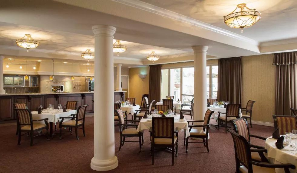 A spacious dining area with elegant decor, featuring tables and chairs arranged symmetrically around classic pillars.