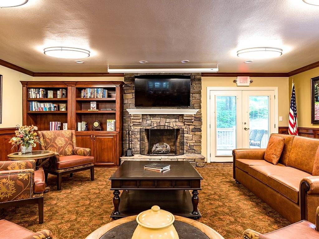 A cozy living room with a fireplace, surrounded by bookshelves, comfortable furniture, and a television mounted above the mantle.