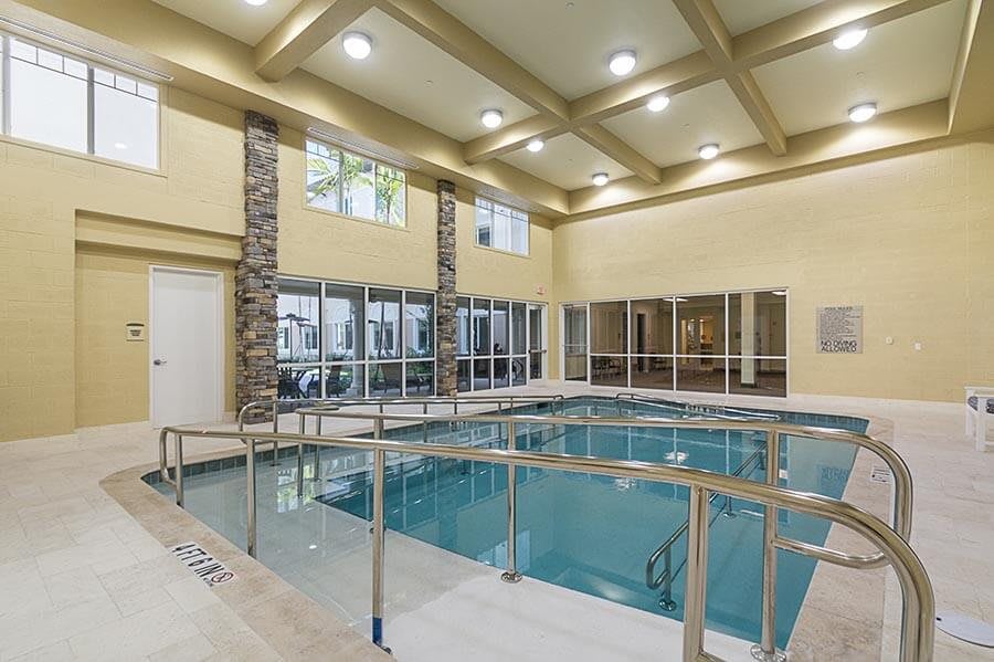A modern indoor swimming pool with glass walls and ample lighting.