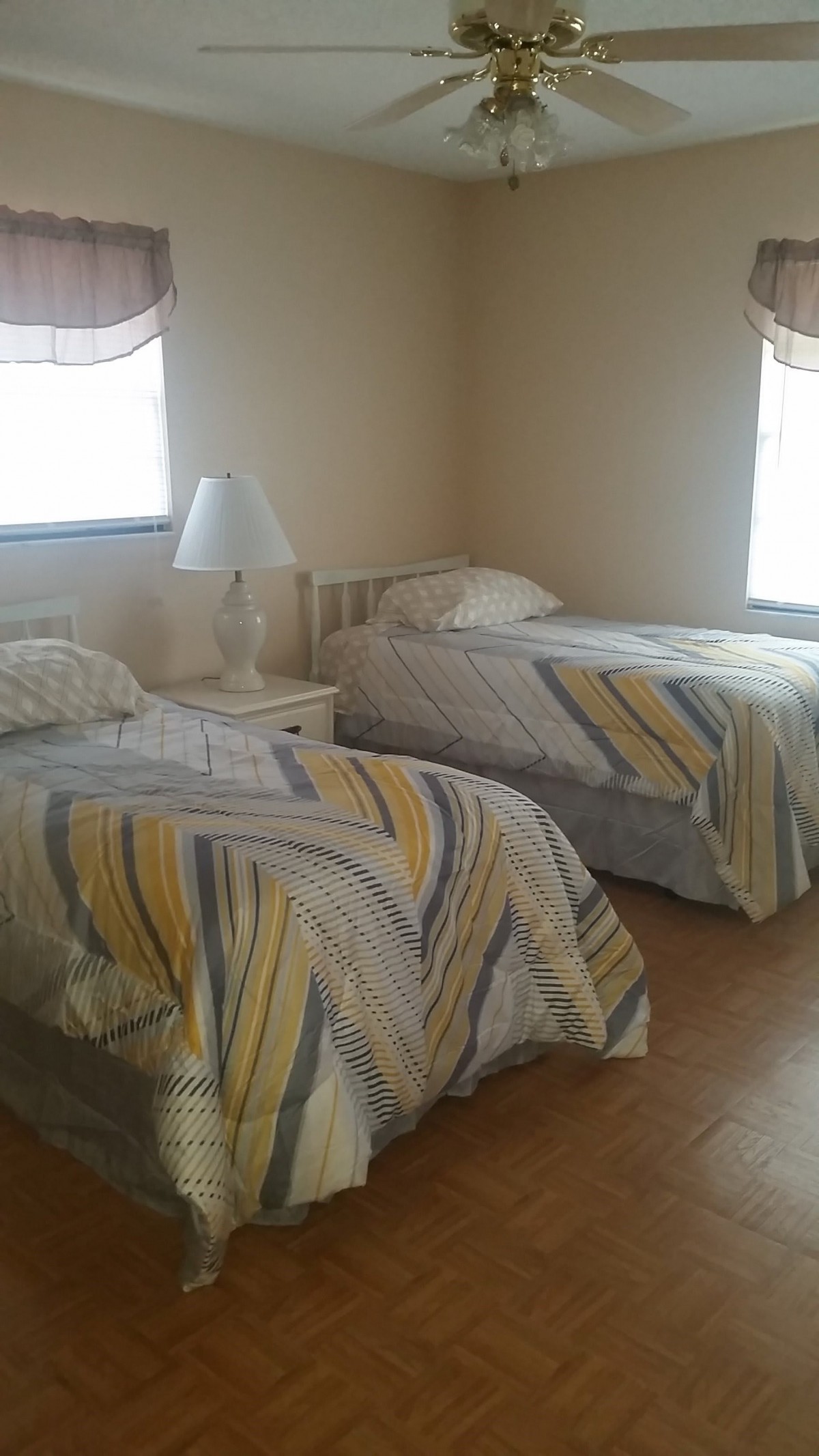 A bedroom with two twin beds, each covered with patterned blankets, and a lamp on a nightstand between them.