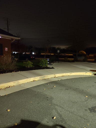 A quiet evening scene showing a sidewalk and parking area under dim lighting.