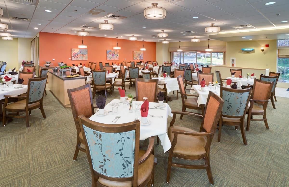 A spacious dining area with multiple tables and chairs, elegantly set for a meal, under softly lit ceiling lights.