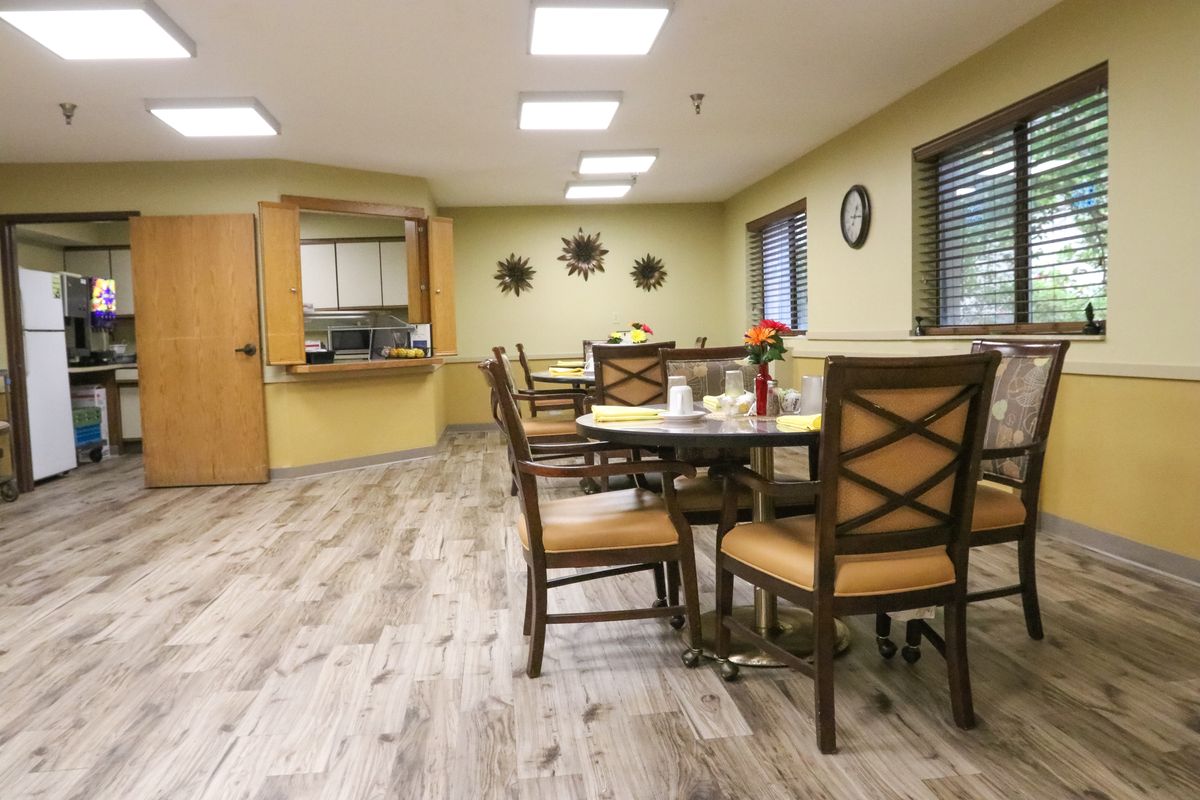 A cozy dining area with wooden tables and chairs, featuring a small kitchenette in the background.